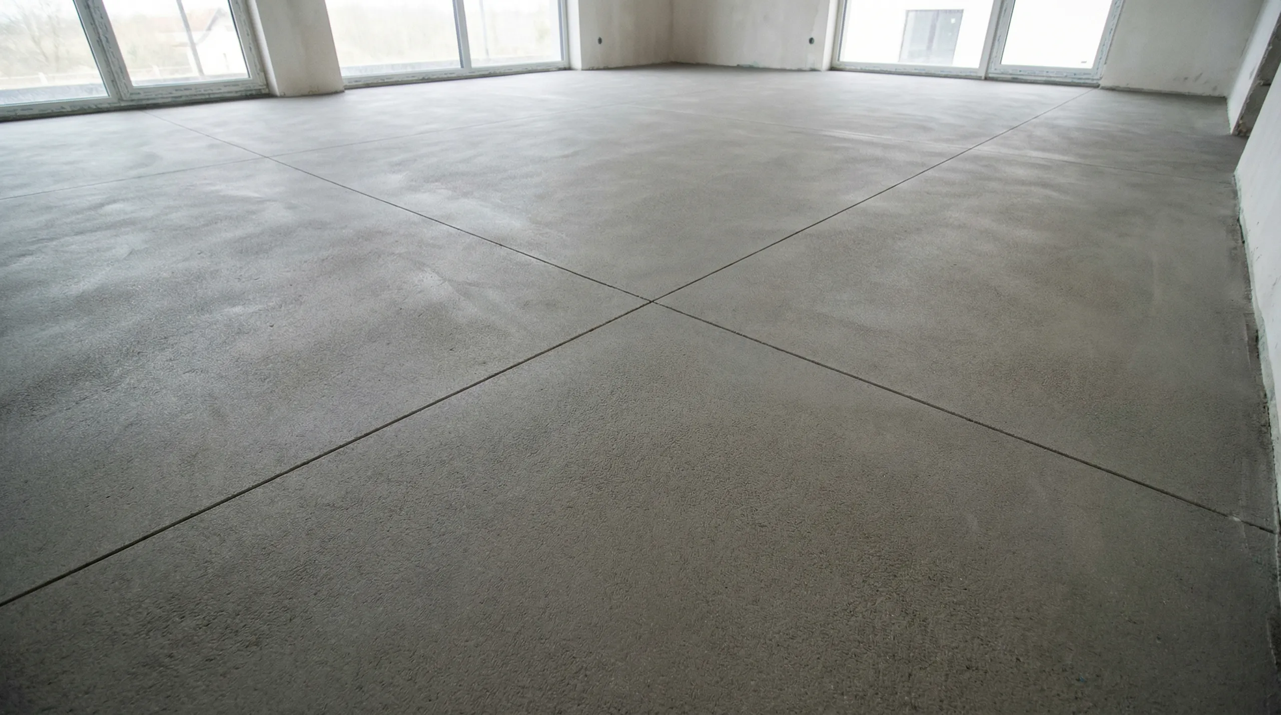 Gładka wylewka betonowa z widocznymi dylatacjami w pomieszczeniu z dużymi przeszklonymi oknami